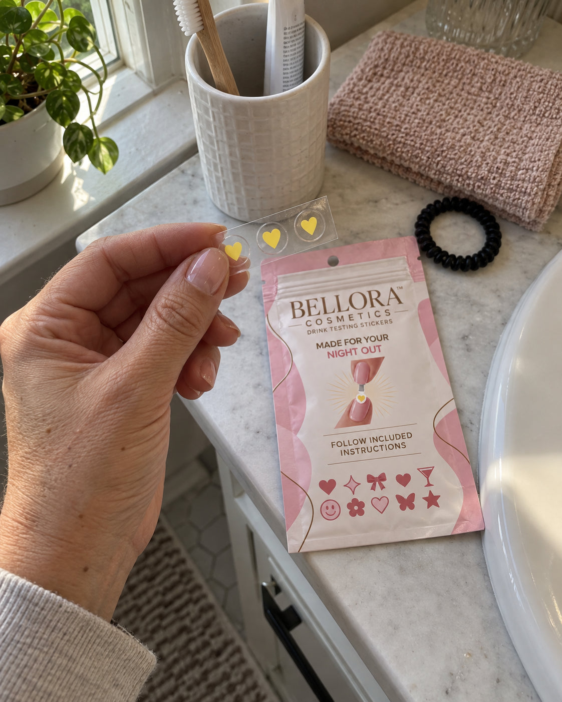 Hand holding three yellow heart stickers above a Bellora packet on a bathroom counter
